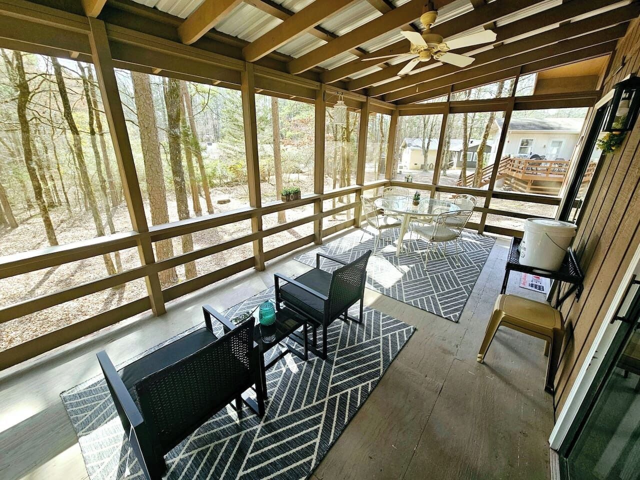 Ein überdachter Außenbereich mit Tisch und Stühlen, einem Deckenventilator und Blick auf den umliegenden Wald.