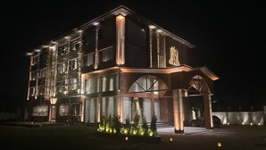 A multi-story hotel with a prominent 'M' logo, large windows, and a well-lit entrance area. - WelcomHeritage Grand Srinagar (Srinagar)