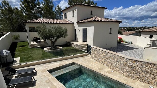 Una casa moderna con piscina, mobiliario de exterior y un jardín cuidado.