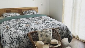 Un dormitorio con una cama, una cesta de mimbre con sombreros, una decoración con forma de corazón, un espejo redondo y un certificado enmarcado en la pared.