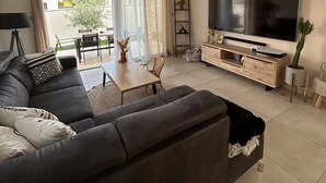 Una sala moderna con un televisor de pantalla plana grande, un sofá oscuro, una mesa de centro de madera y una zona de comedor con una mesa y sillas.