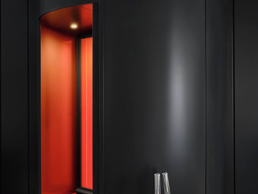 A modern, minimalist room with a curved black wall, a red carpeted area, and a metallic chair.
