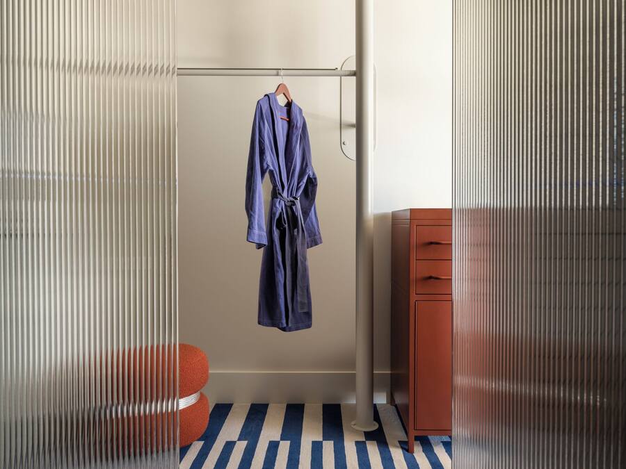 A bathroom with a striped floor, a hanging robe, and a wooden cabinet.