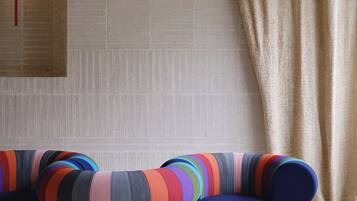 A modern living room with a sofa featuring colorful stripes, a blue ottoman, and a beige curtain.