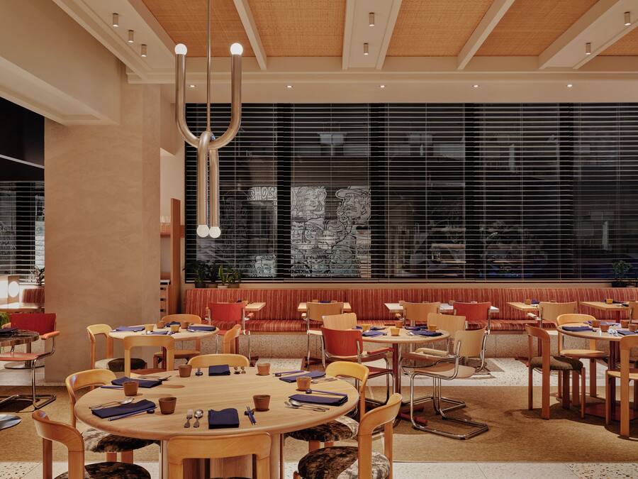 Un comedor moderno con mesas y sillas redondas, ventanas amplias con persianas e iluminación empotrada en el techo.
