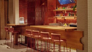 Zona de bar con una barra alargada, varios taburetes y un rebozo de azulejos.