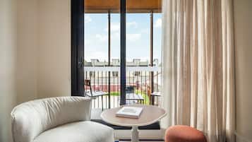 A room with a view of a balcony, a round table with a book, a white chair, and a red ottoman.