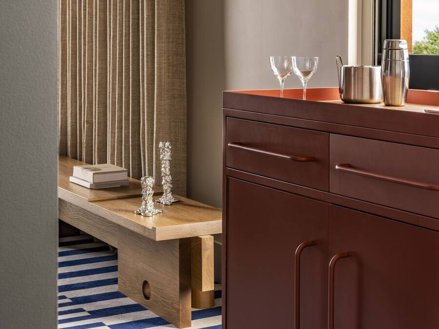 Una habitación moderna con un banco de madera, un mueble marrón y dos vasos transparentes en un alféizar.