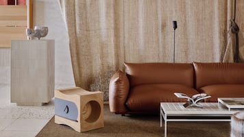 A modern living room with a brown leather sofa, a wooden side table, a white coffee table, and a large window with a curtain.