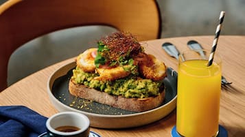 Un plato de desayuno con tostada de aguacate, un vaso de jugo de naranja y una taza de café sobre una mesa de madera.