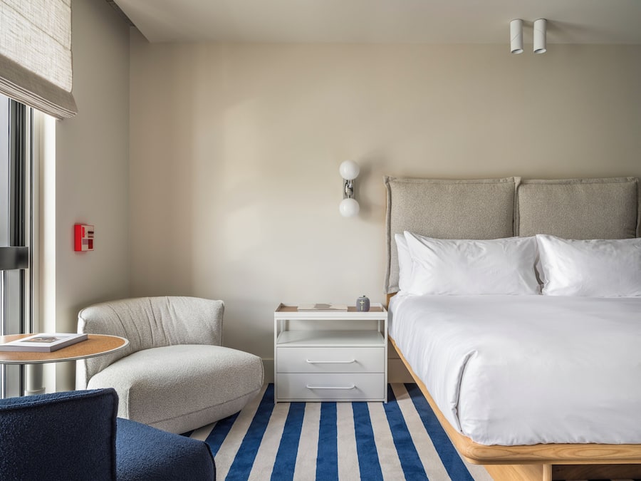 Een moderne hotelkamer met een groot bed, een klein zithoekje, een nachtkastje en een raam met zonwering.