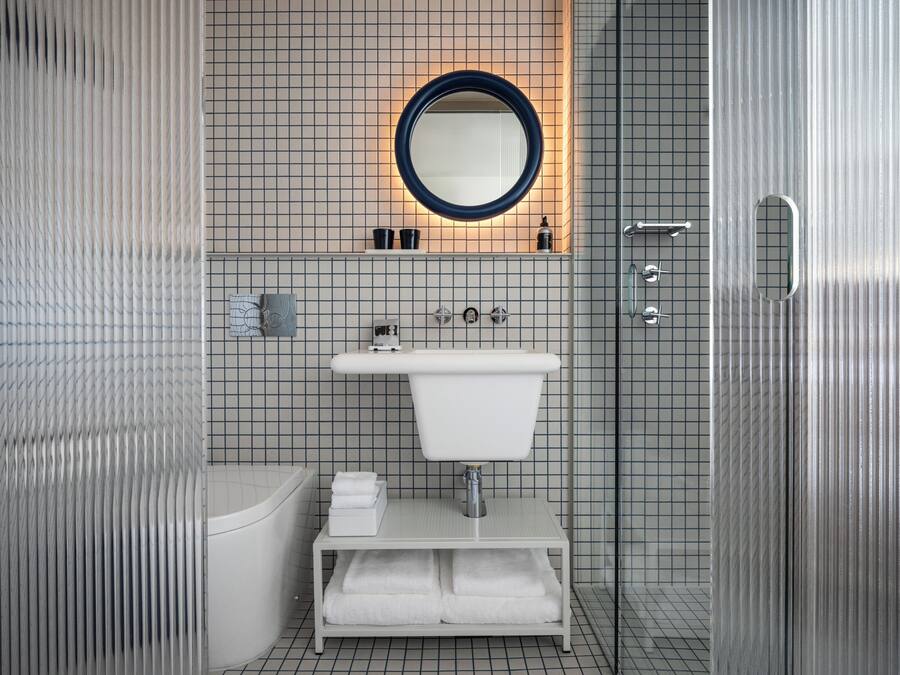 Een moderne badkamer met een wit wastafel, een ronde spiegel, een badkuip en een douchehoek.