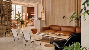 Una sala de estar con un sofá de cuero marrón, sillones blancos, una mesa de centro y un ventanal con cortinas.