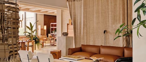 A living room with a brown leather sofa, white armchairs, a coffee table, and a large window with curtains.