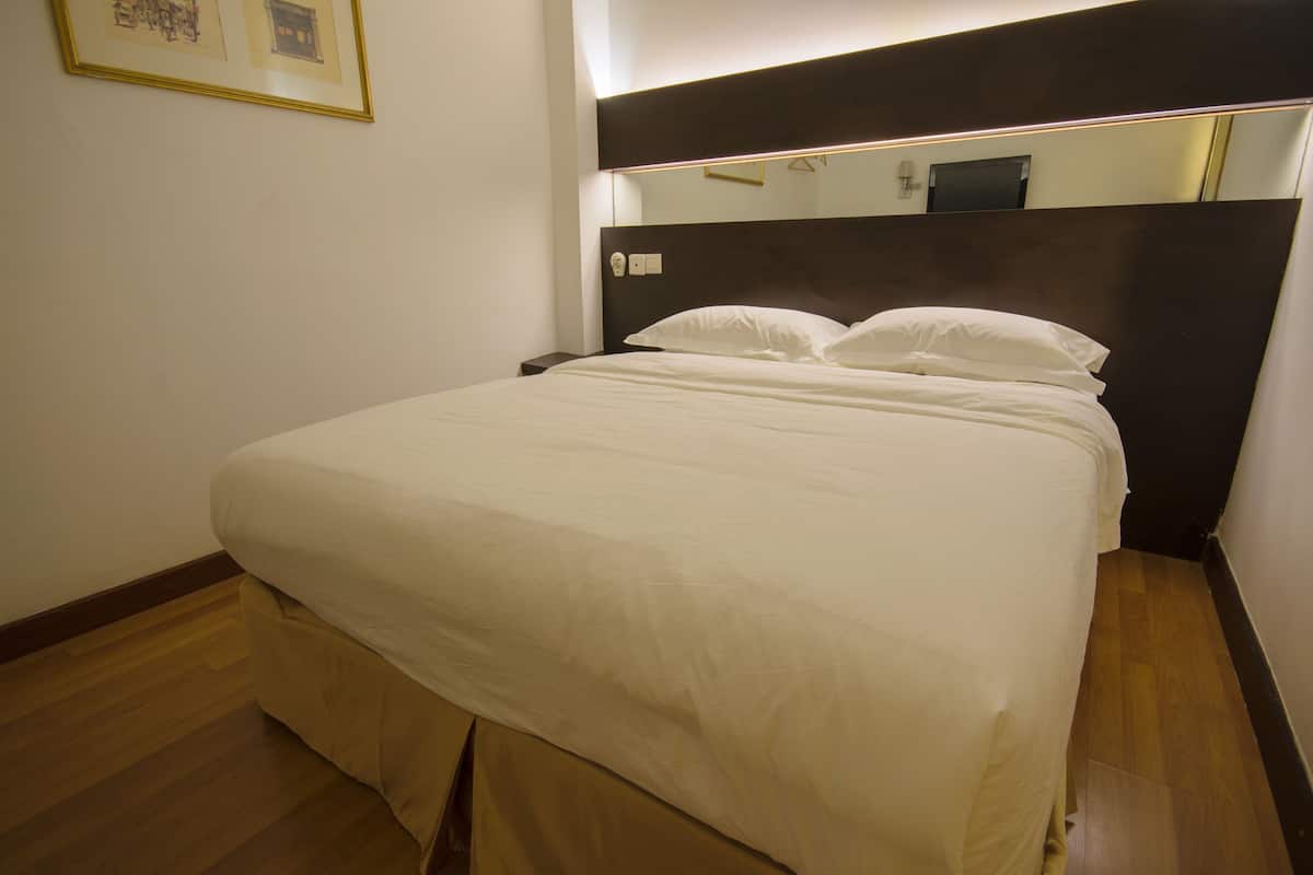 A neatly made bed in a hotel room with a wooden floor and a dark headboard.