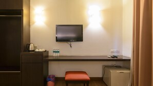 Una kitchenette compacta con una televisión de pantalla plana sobre una encimera, un refrigerador pequeño, un banco y un cubo de basura.