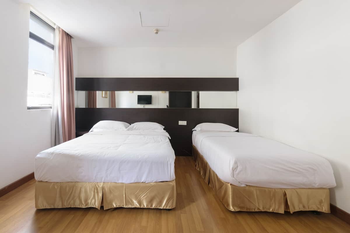 A hotel room with two single beds, a large mirror, a flat-screen TV, and a window with curtains.