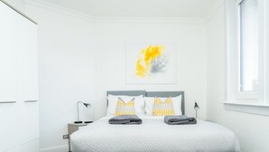 A modern bedroom with a large bed, two bedside tables, a window with blinds, and a wall-mounted abstract art piece. - Haywood by Central Serviced Apartments (Dundee City Council)