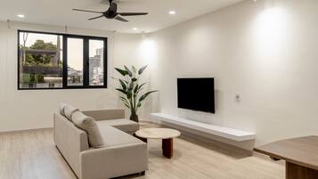 Una sala de estar moderna con un sofá, una mesa de centro, un televisor montado en la pared y un ventanal con vistas a la ciudad.