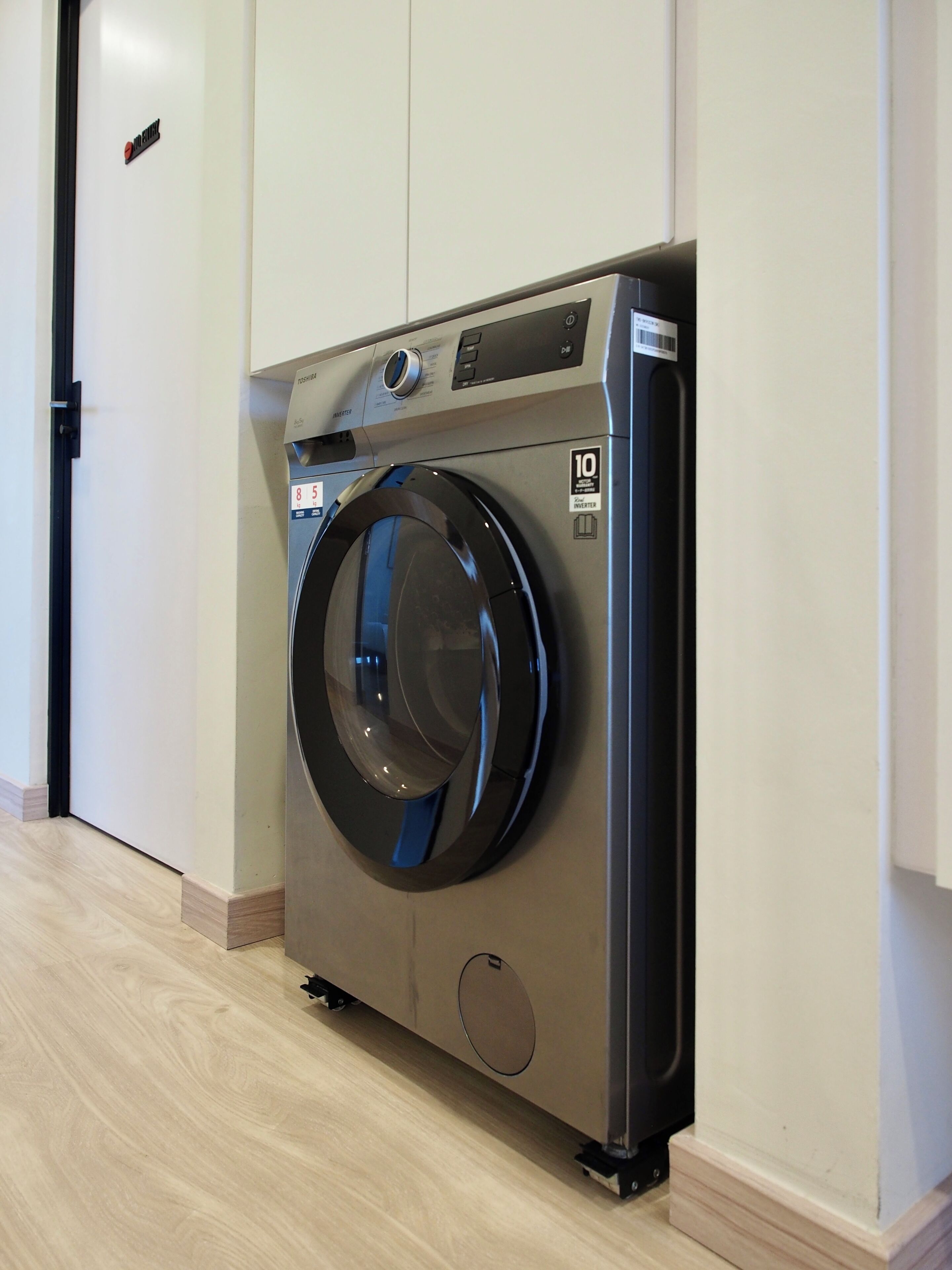 Een voorlader wasmachine in een hotelkamer met een houten vloer en witte muren.