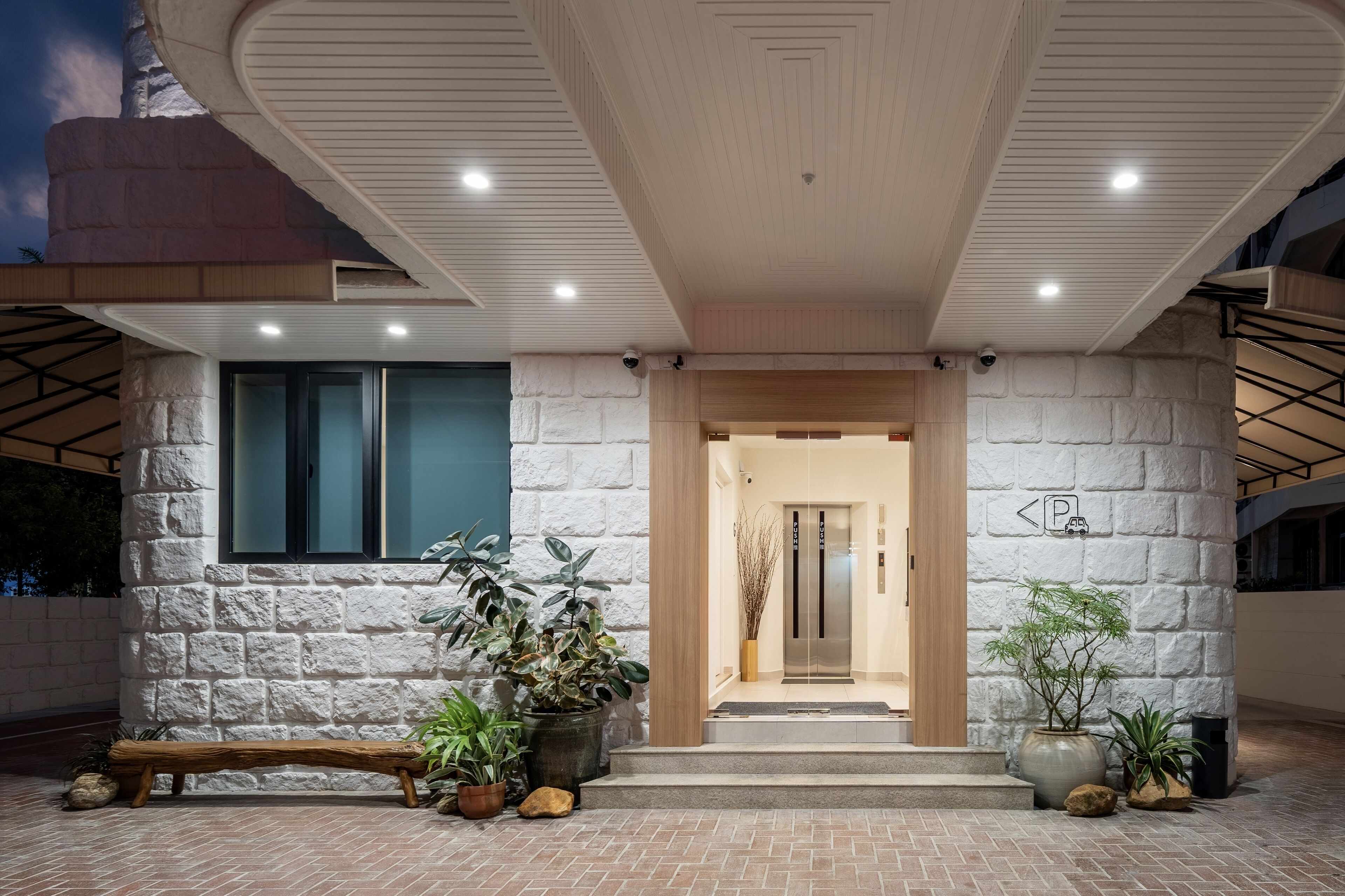 A modern building entrance with a stone facade, a wooden bench, and potted plants.