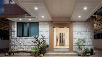Entrada de un edificio moderno con fachada de piedra, un banco de madera y plantas en macetas.
