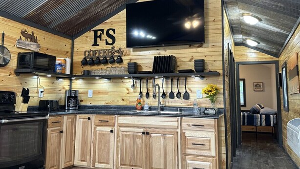 A compact kitchen with wooden cabinets, a large TV, and various kitchen utensils hanging on the wall. - FS Rental #4 Annapolis, MO Black River (Annapolis)