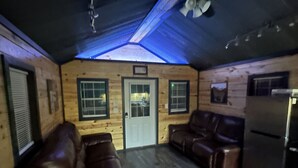 A log cabin interior with a wooden floor, two leather sofas, a refrigerator, and a door with windows. - FS Rental #4 Annapolis, MO Black River (Annapolis)