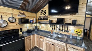 A modern kitchen with wooden cabinets, a black countertop, a stove, and a large TV mounted on the wall. - FS Rental #4 Annapolis, MO Black River (Annapolis)
