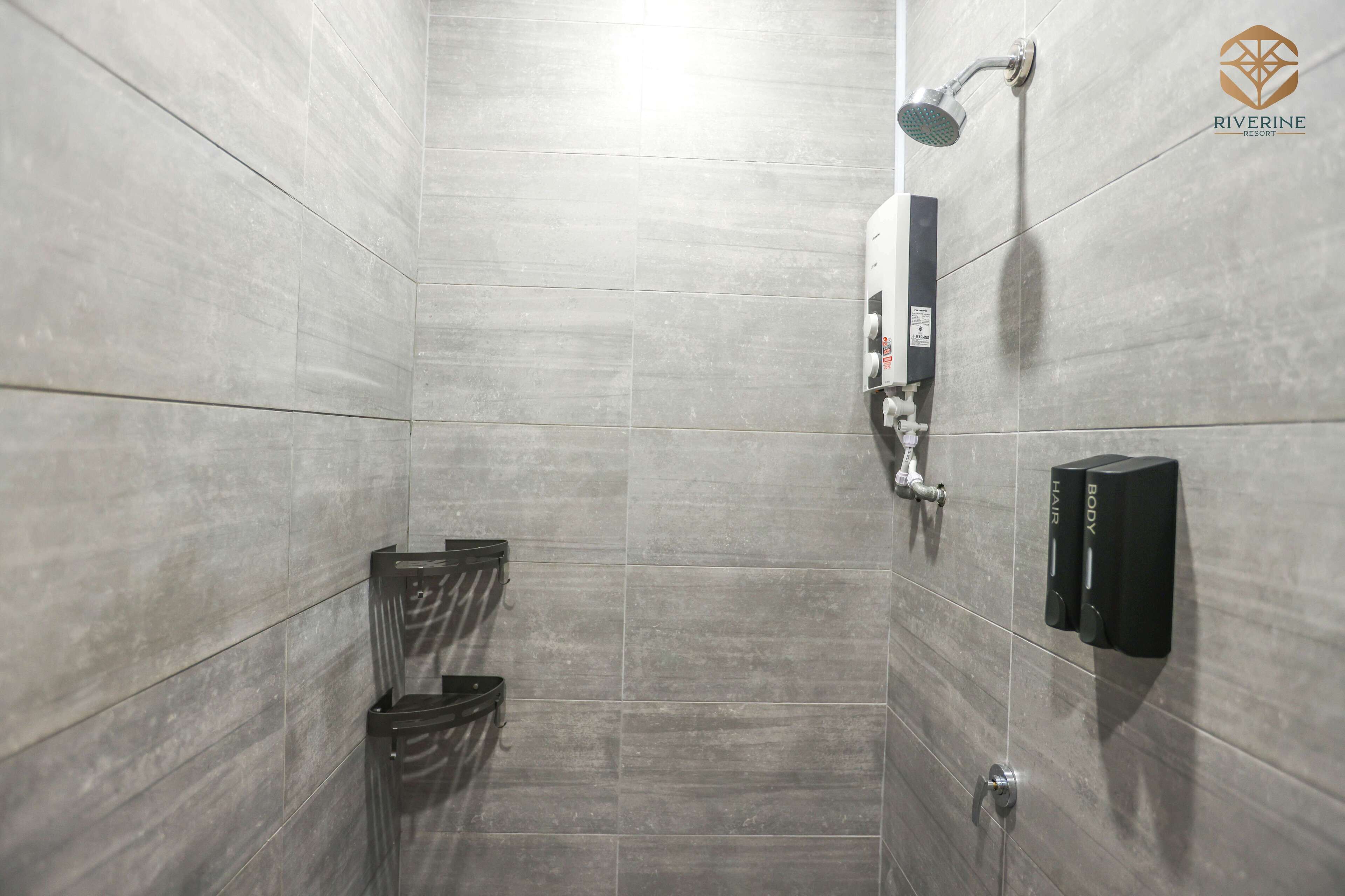 A modern shower area with grey tiles, a handheld showerhead, and a black soap dispenser.