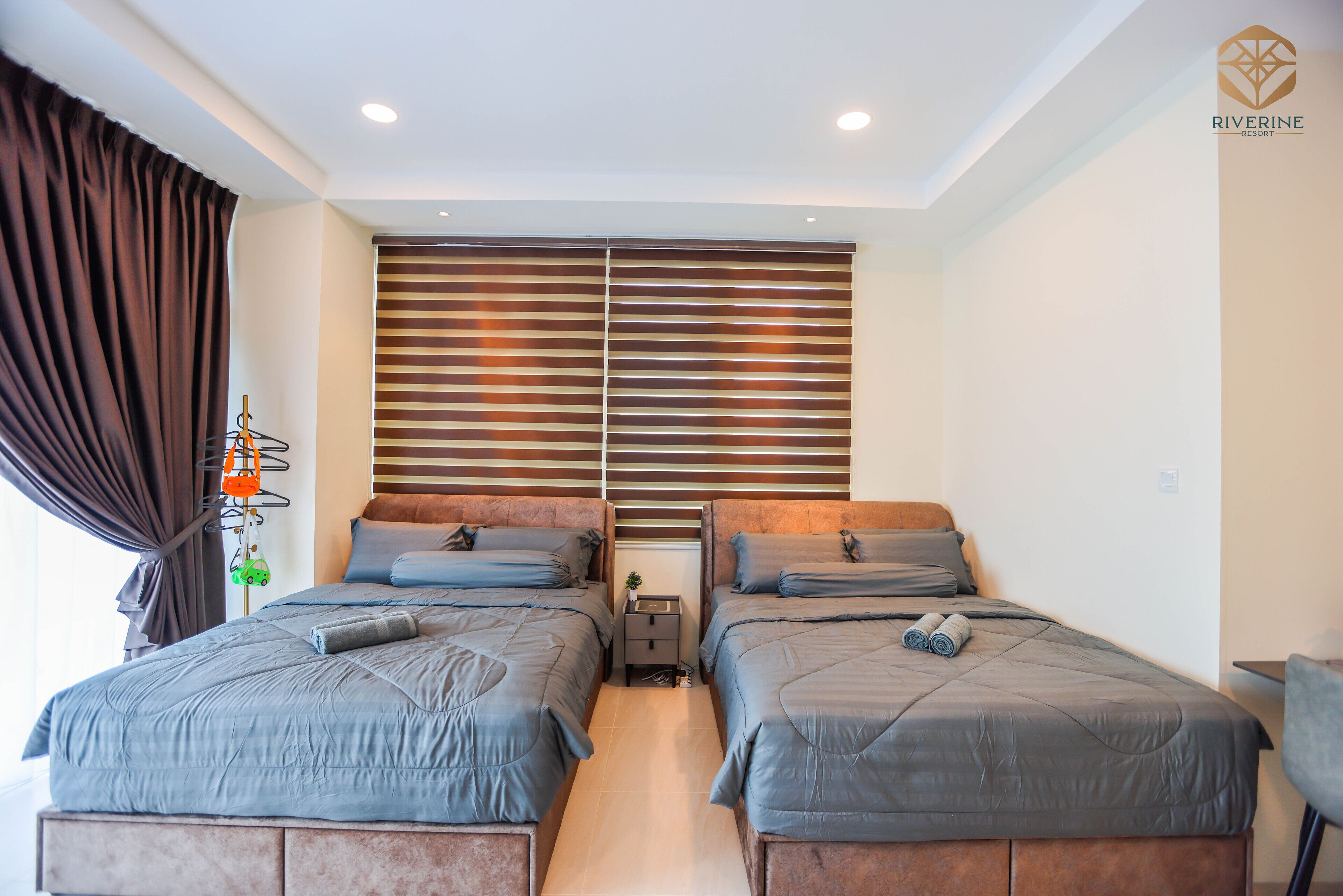 A bedroom with two beds, a nightstand, and a window with blinds.