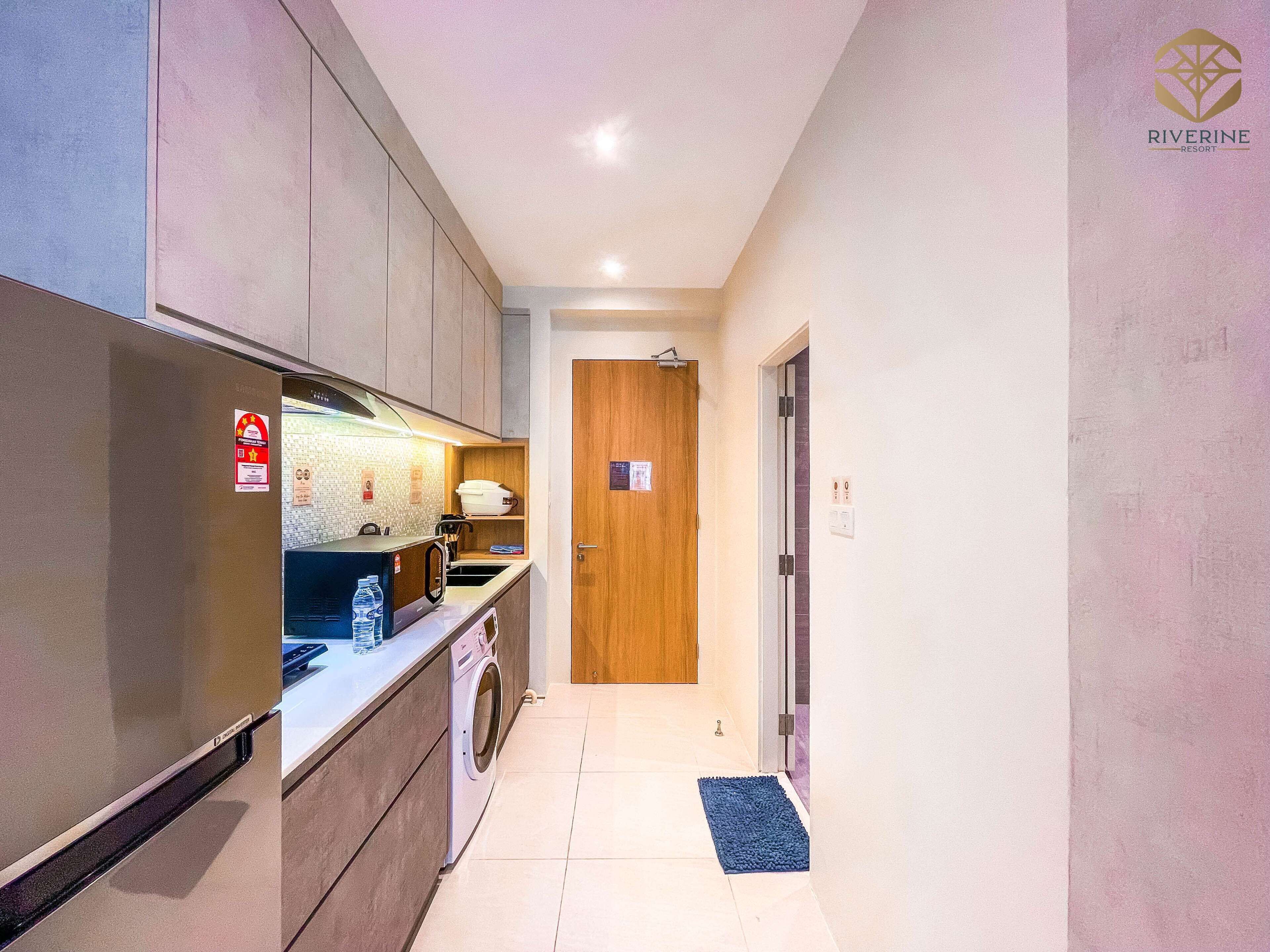 Un pasillo estrecho con una zona de cocina a un lado, que incluye un refrigerador, microondas y lavadora.