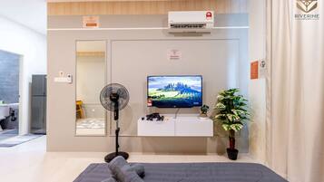 Une chambre d’hôtel moderne équipée d’un téléviseur à écran plat, d’un ventilateur sur pied, d’une plante en pot et d’un lit avec des couvertures pliées.
