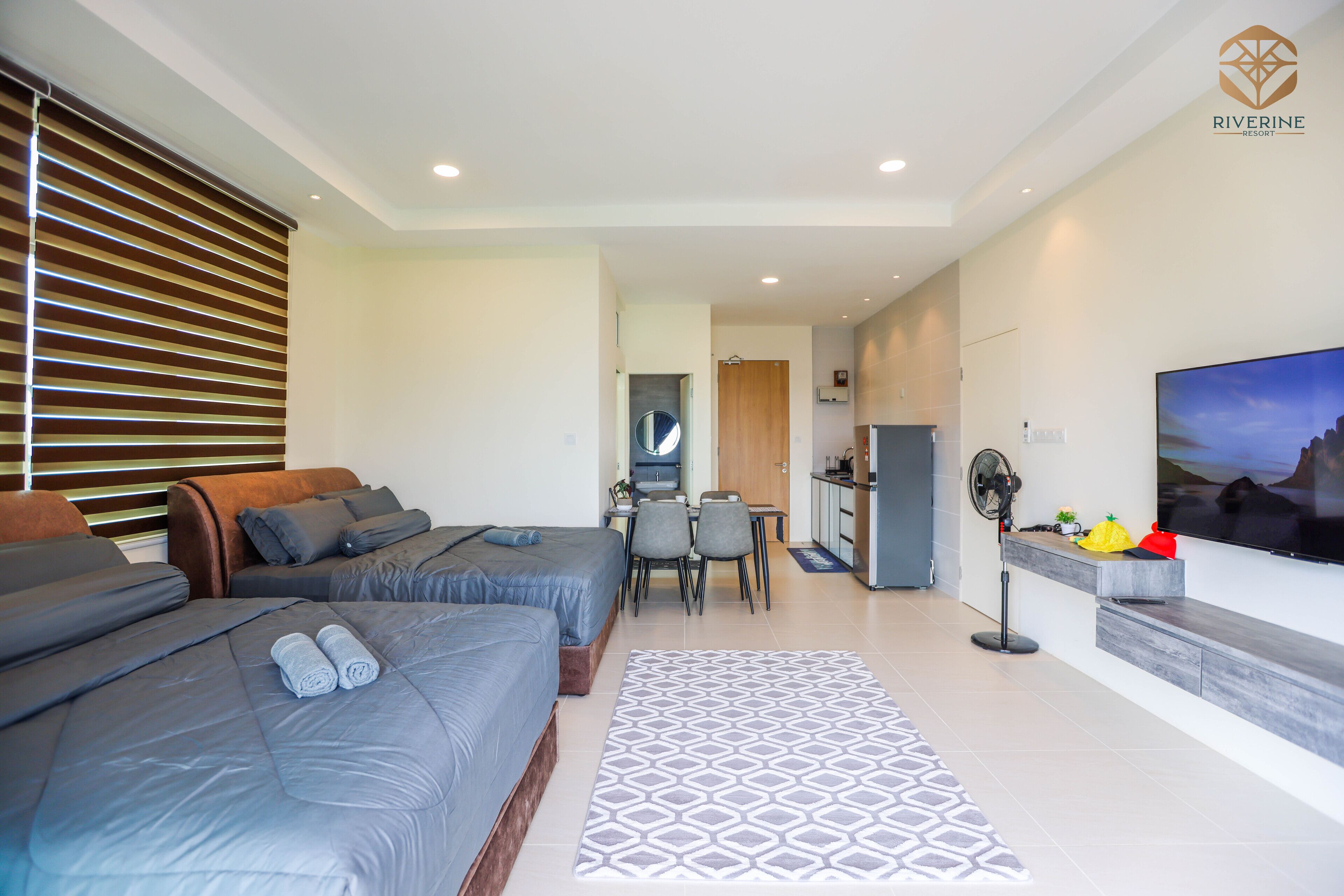 A modern hotel room with two beds, a dining area, and a TV.