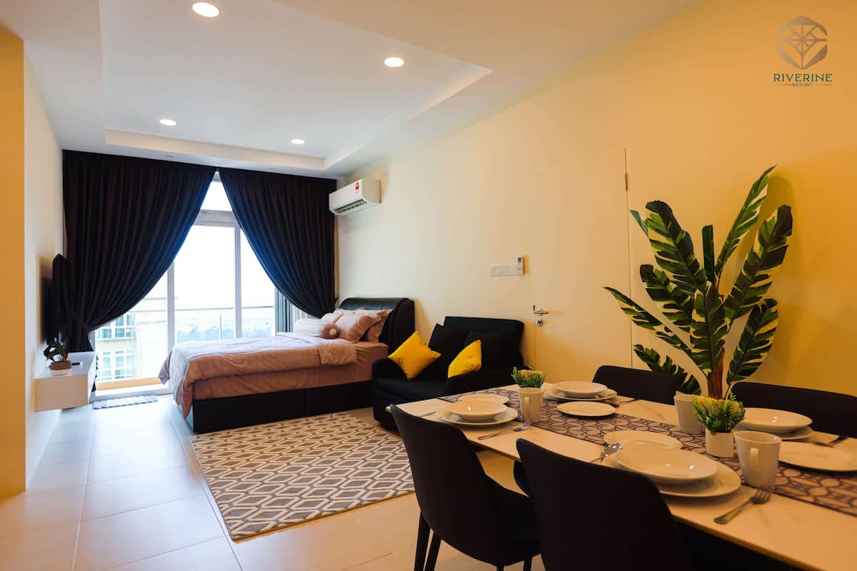 A modern hotel room with a bed, a dining area with a table set for two, and a large window with curtains.