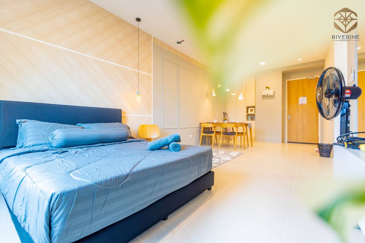 A modern hotel room with a large bed, a dining area, and a fan.