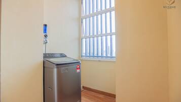 A compact room with a washing machine, a window with blinds, and a visible Riverine Resort logo.