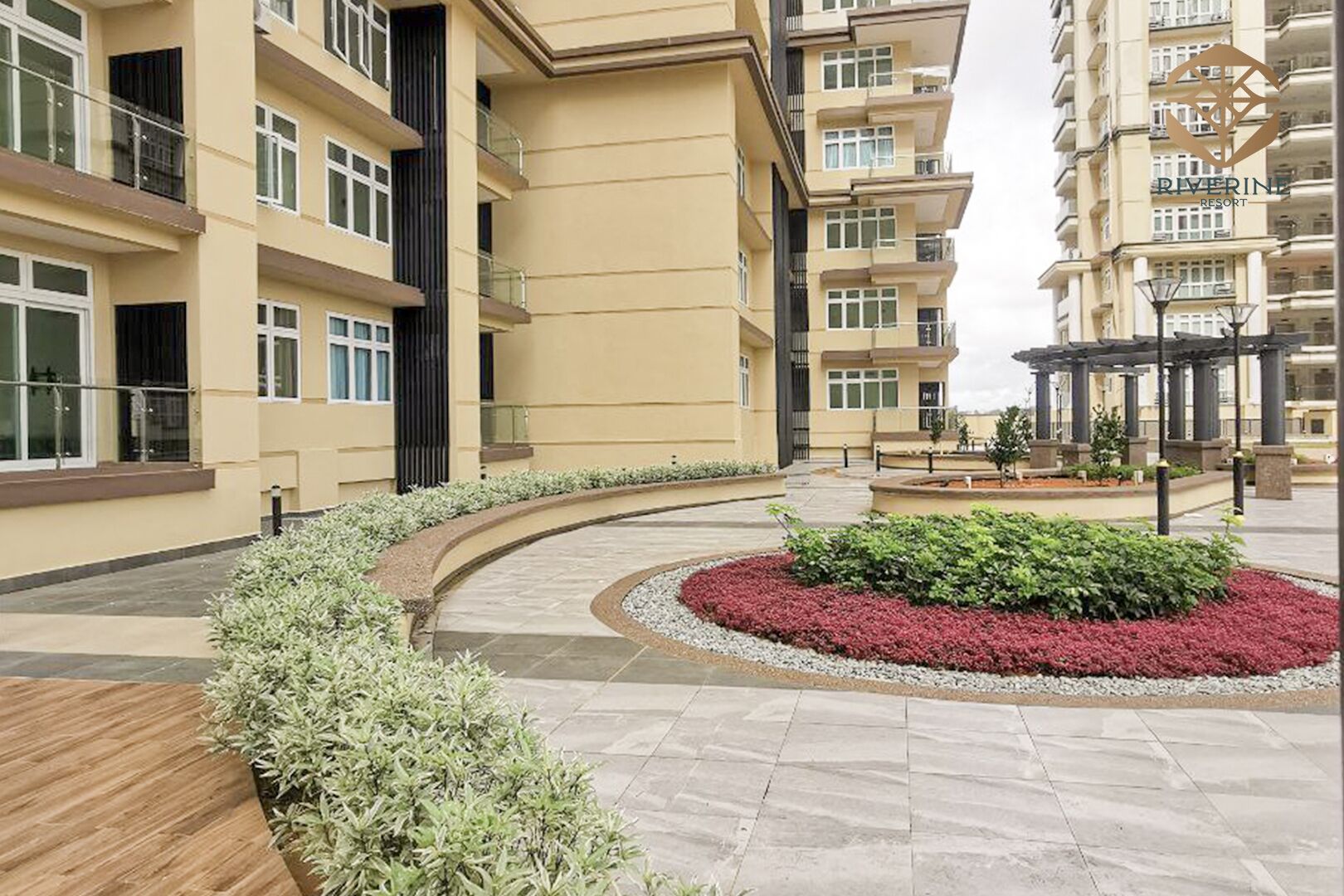 Un edificio residencial moderno con varios balcones, un patio ajardinado con un jardín circular y una estructura de pérgola.