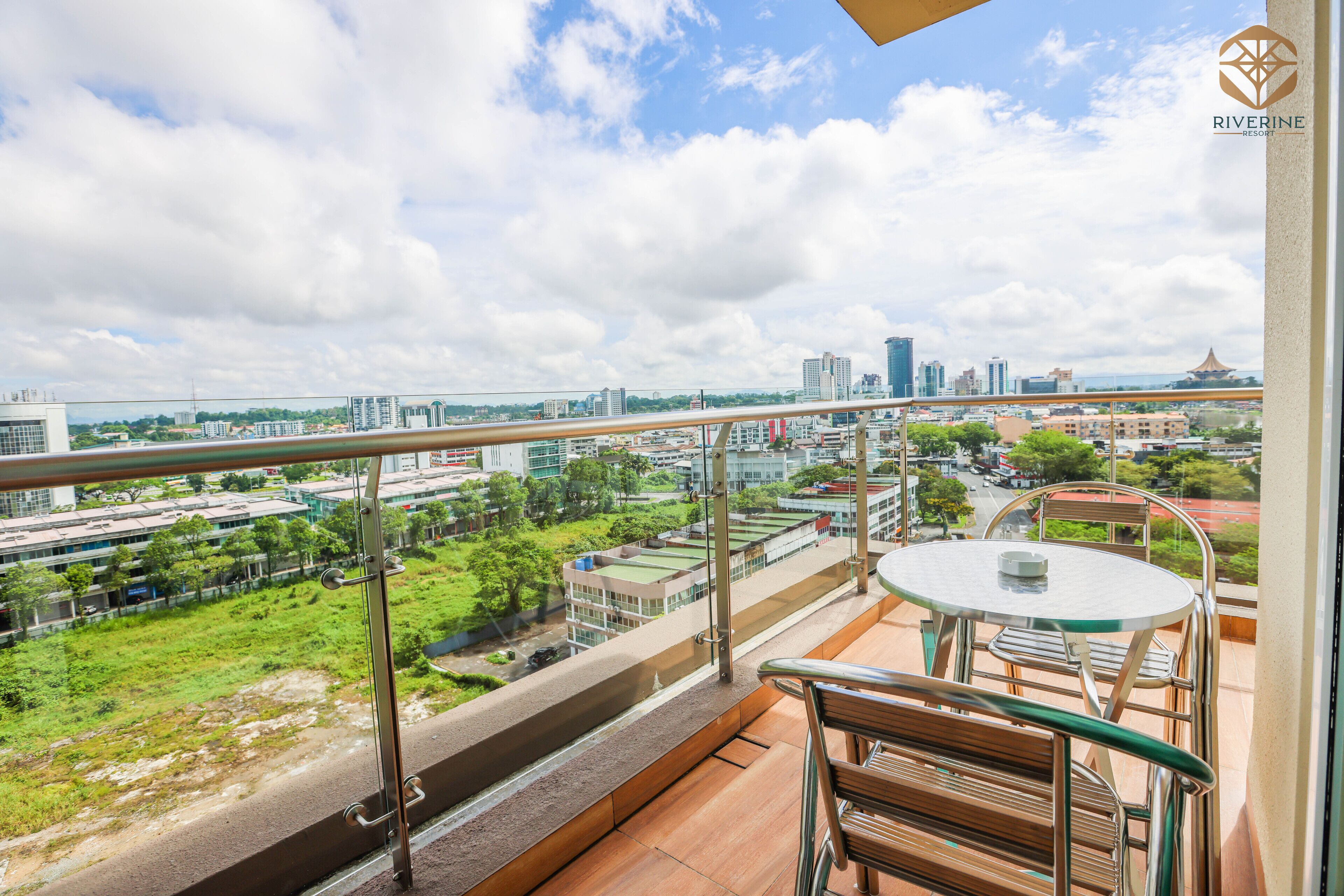 A balcony with a table and chairs, overlooking a cityscape with buildings and greenery.