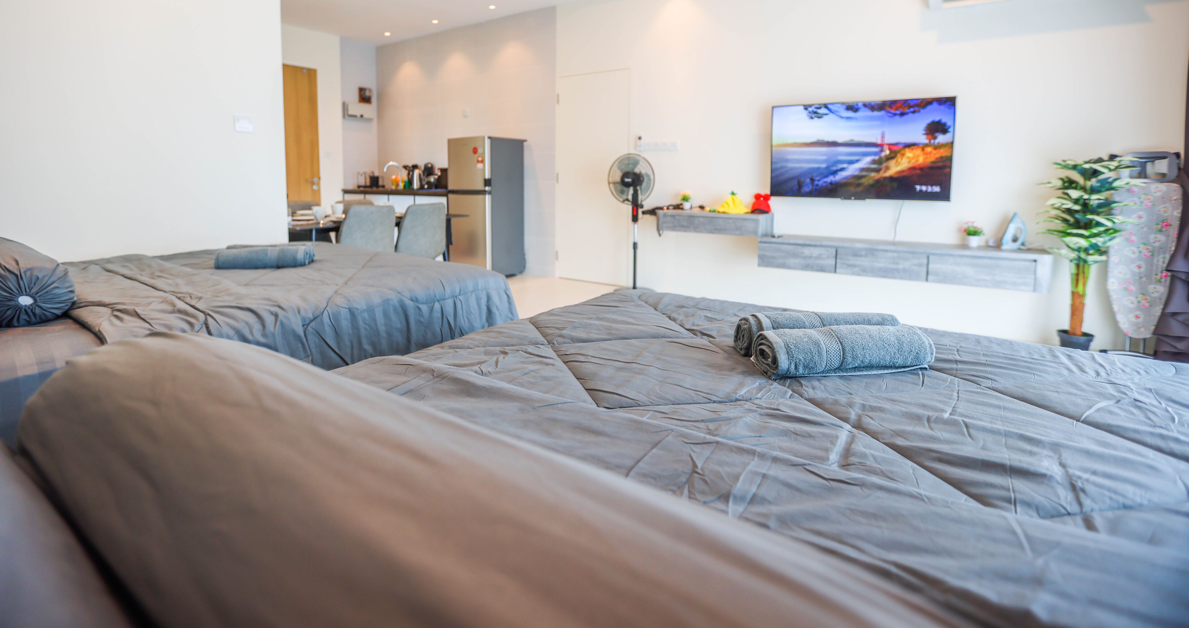 A modern hotel room with two beds, a TV, a small kitchenette, and a dining area.