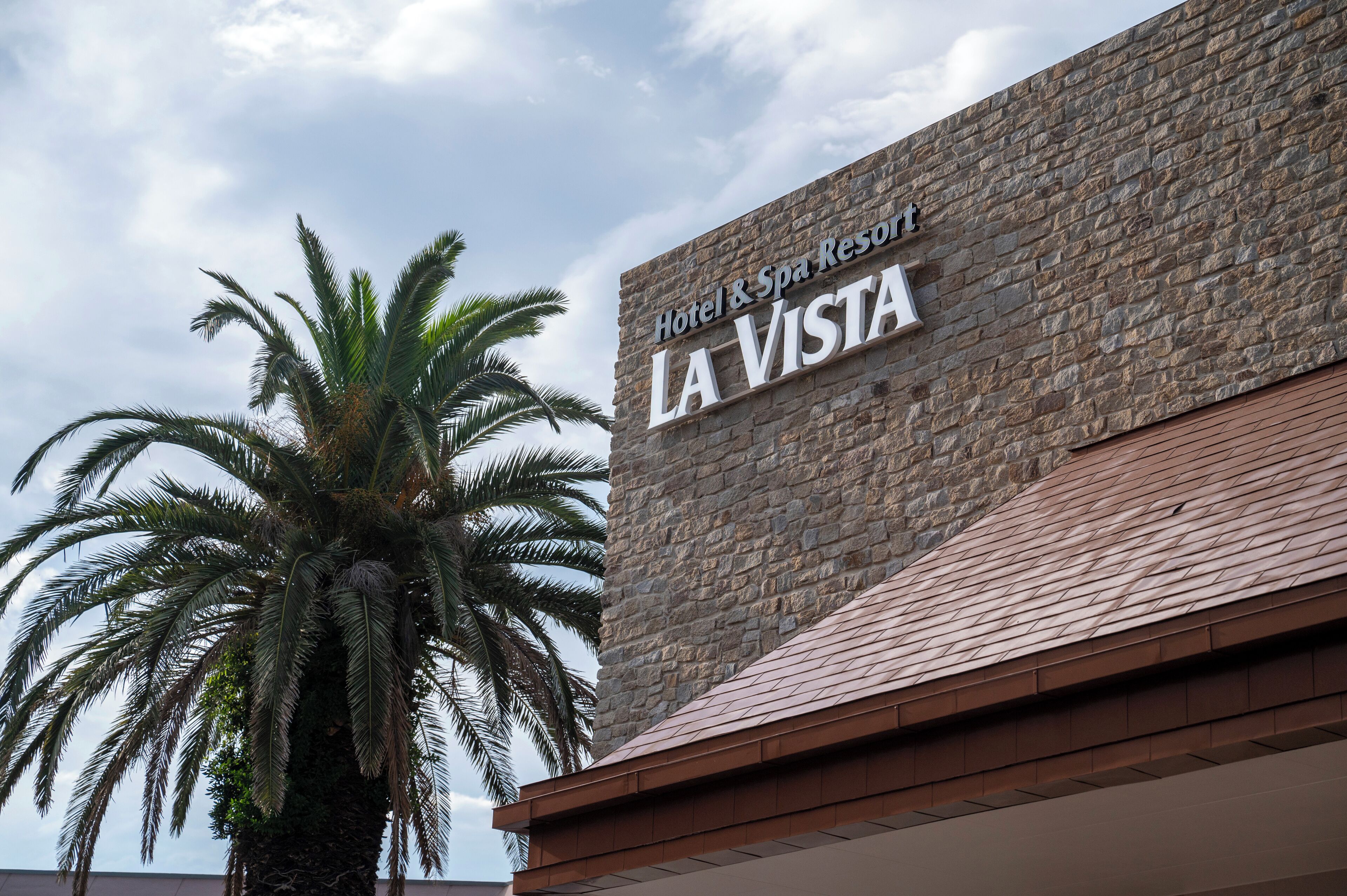 A sign for Hotel & Spa Resort La Vista with a stone facade and a palm tree in the foreground.
