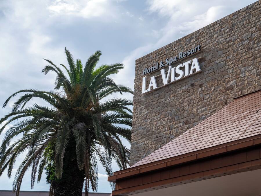 A sign for Hotel & Spa Resort La Vista with a stone facade and a palm tree in the foreground.