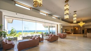 A spacious lobby with multiple seating areas, large windows offering ocean views, and elegant chandeliers.