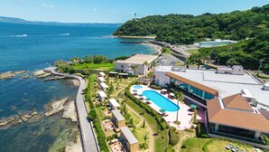 An aerial view of a coastal resort with a swimming pool, guest villas, and a beach access area.