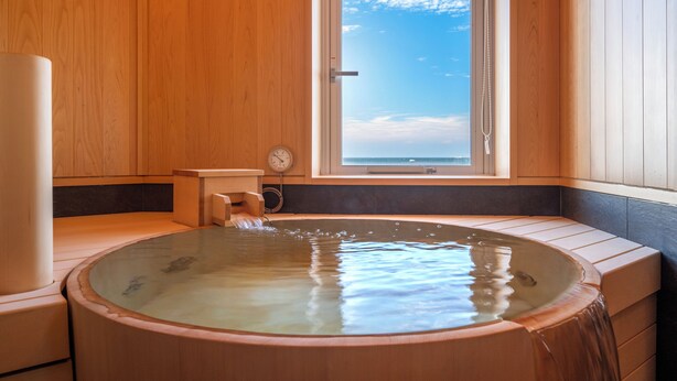 A wooden sauna with a large window, a wooden bench, and a water feature.