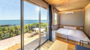 A bedroom with a large window overlooking a scenic view, a bed, a small table, and a chair.