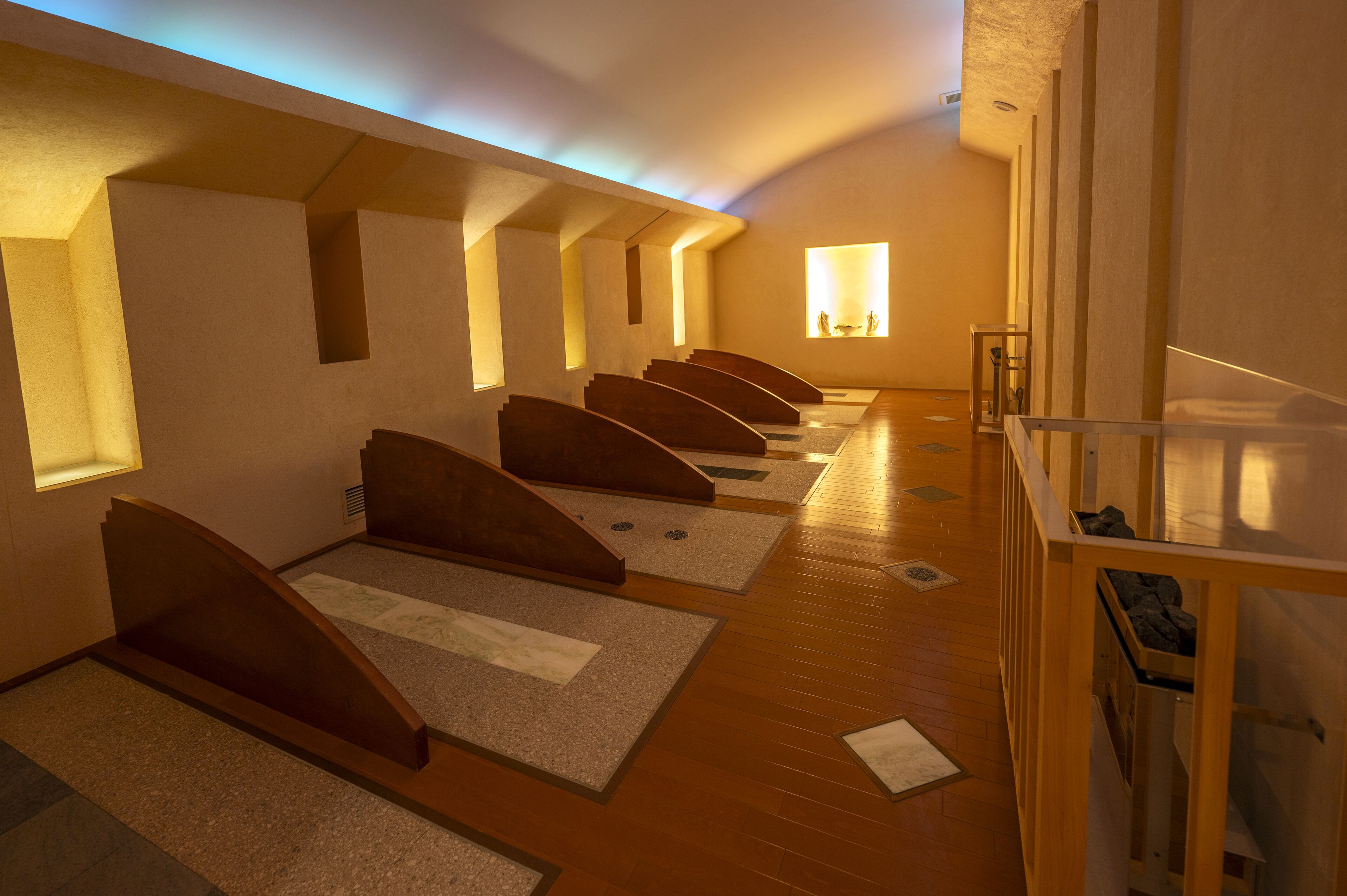 Ein Zimmer mit mehreren nebeneinanderliegenden Betten, Holzböden und einem kleinen Fenster, das natürliches Licht hereinlässt.