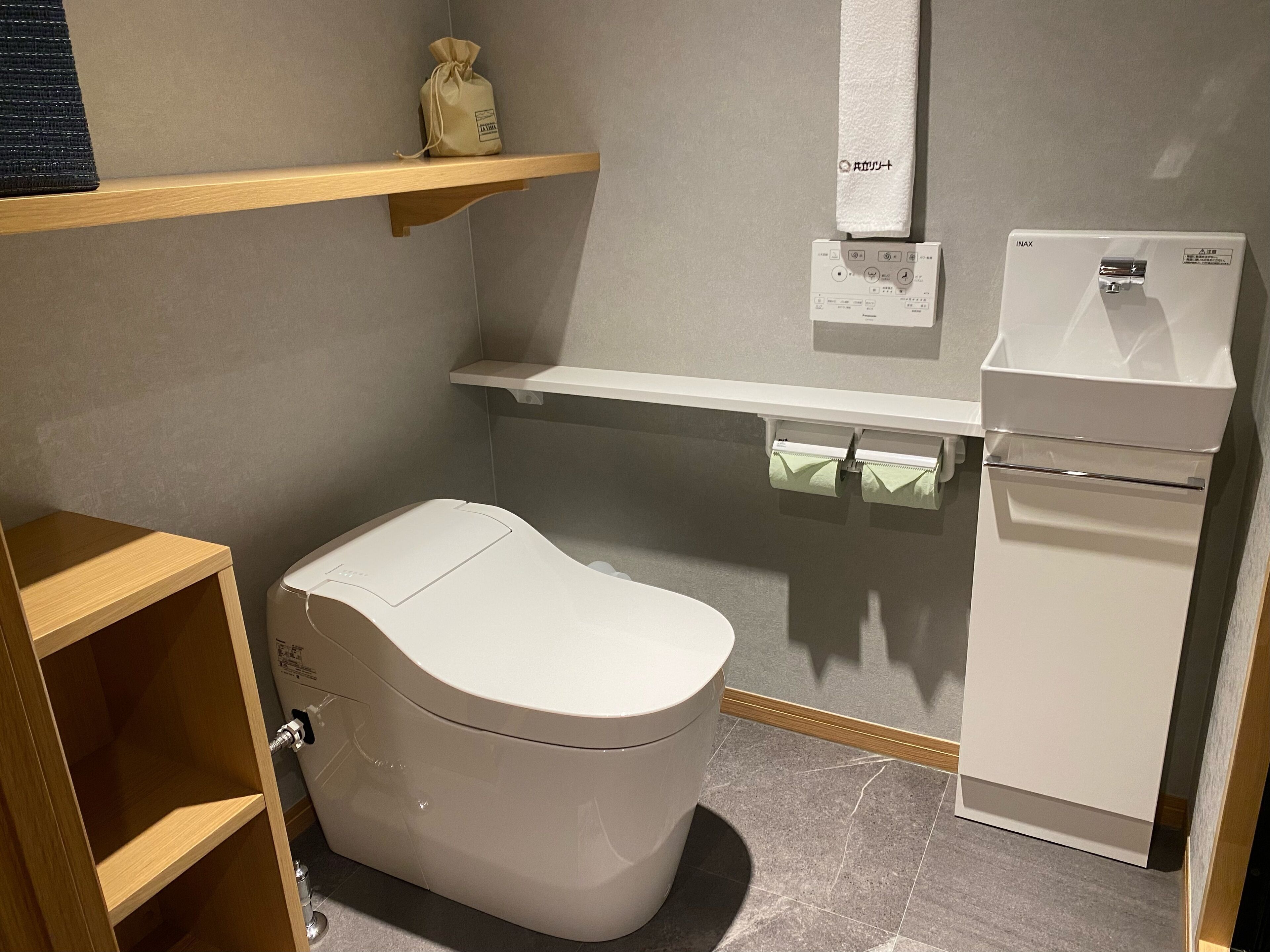 A modern bathroom with a toilet, a sink, and a shelf with a bag.
