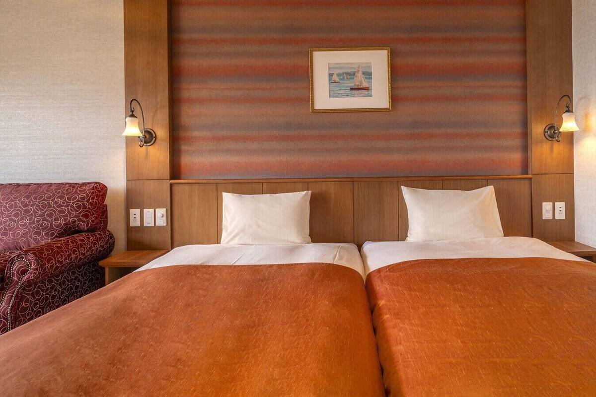 Habitació d'hotel amb dos llits, un panell frontal de fusta, un quadre amb marc a la paret i dues làmpades penjades a la pared.