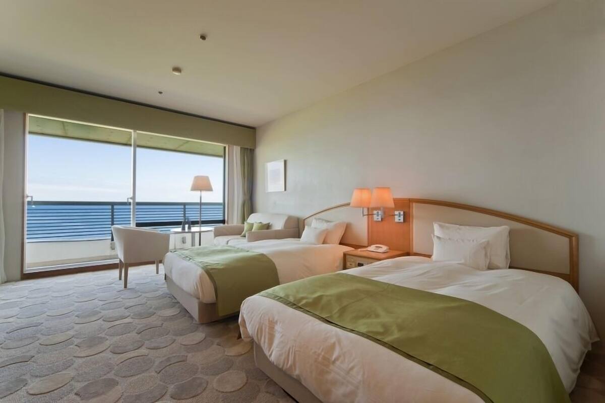 Habitació d'hotel amb dos llits, un sofà, una cadira, escriptori i vista al mar.